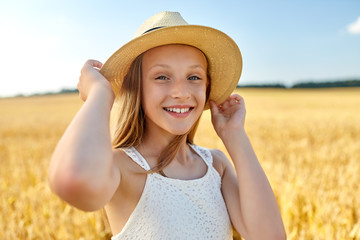 nature, fashion and people concept - portrait of smiling young girl in straw hat on cereal field in summer