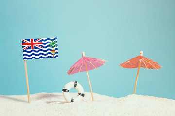 Miniature flag of British Indian Ocean Territory on beach with colorful umbrellas and life preserver. Travel concept, summer theme.