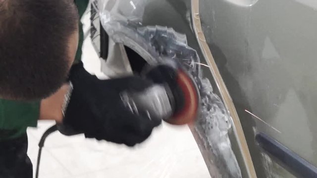 Close-up of worker grinds car damage. Stock footage. Professional auto workshop worker grinds dented front fender of car. Hard grinding is designed to smooth out irregularities
