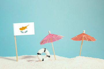 Miniature flag of Cyprus on beach with colorful umbrellas and life preserver. Travel concept, summer theme.