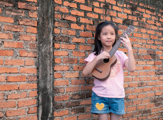 Little asian child play the ukulele, old brick wall background