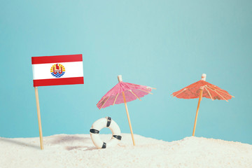 Miniature flag of French Polynesia on beach with colorful umbrellas and life preserver. Travel concept, summer theme.