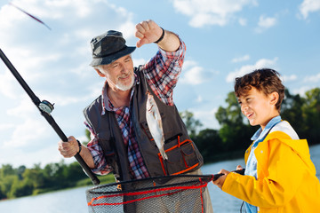 Handsome young excited boy fishing with granddad
