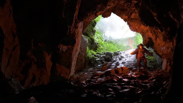 Hiker down into cave. Stock footage. Traveler with red signal candle descends into cave on slope on background of arched entrance