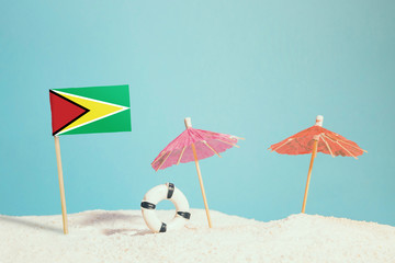 Miniature flag of Guyana on beach with colorful umbrellas and life preserver. Travel concept, summer theme.