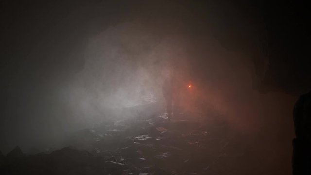 Traveler with torch in dark cave. Stock footage. Man with torch is selected from dark misty cave. Silhouette of man with weak torch climbs on stones to top in pitch darkness of cave