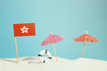 Miniature flag of Hong Kong on beach with colorful umbrellas and life preserver. Travel concept, summer theme.