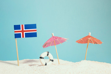 Miniature flag of Iceland on beach with colorful umbrellas and life preserver. Travel concept, summer theme.