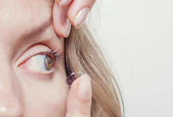 Woman inserts a contact lens into the eye.