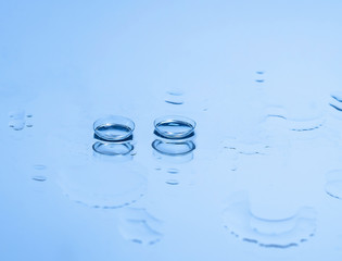 Contact lenses for the eyes on the glass among the drops of water in blue. Optical equipment, good...