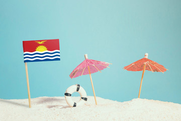 Miniature flag of Kiribati on beach with colorful umbrellas and life preserver. Travel concept, summer theme.