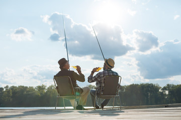 Father and son sitting in chairs and drinking beer while fishing