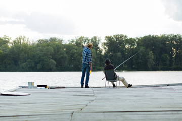 Man wearing hat talking to father sitting and catching fish