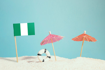 Miniature flag of Nigeria on beach with colorful umbrellas and life preserver. Travel concept, summer theme.