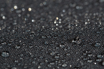 dark gray waterproof hydrophobic flat cloth closeup with rain drops selective focus background