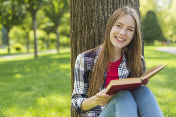 Happy girl reading a book while sitting on grass