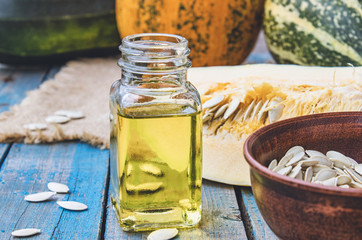 Pumpkin seeds and essential oil in a bottle near the pumpkin on blue old boards.