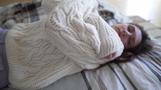 Happy Caucasian young woman basking at home on a cold autumn evening, smiling and looking at the camera. White woolen knitted sweater closeup, hugge concept