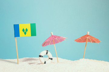 Miniature flag of Saint Vincent And The Grenadines on beach with colorful umbrellas and life preserver. Travel concept, summer theme.