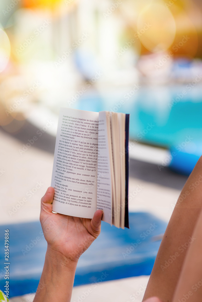 Wall mural woman on vacation reading a book by the pool