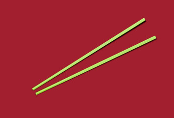 A green pair of chopstick on red background, top view