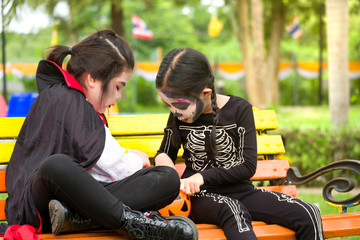Fototapeta na wymiar Little cute girl asia in Halloween costume Is sharing sweets and candies while sitting at the bench in the playground.