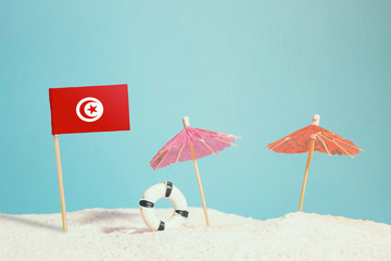 Miniature flag of Tunisia on beach with colorful umbrellas and life preserver. Travel concept, summer theme.