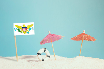 Miniature flag of United States Virgin Islands on beach with colorful umbrellas and life preserver. Travel concept, summer theme.