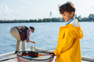 Smiling boy wearing yellow raincoat holding fishing net