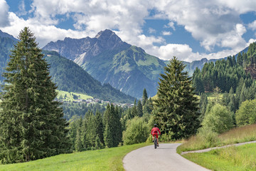 Fototapeta na wymiar nice active senior woman riding her electric mountain bike in the Kleinwalstertak, Vorarlberg, Austria, famous summit of Widderstein in the background