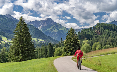 Fototapeta na wymiar nice active senior woman riding her electric mountain bike in the Kleinwalstertak, Vorarlberg, Austria, famous summit of Widderstein in the background
