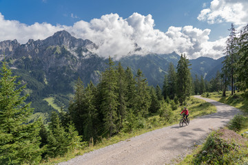 Fototapeta na wymiar nice and active senior woman, riding her e-mountain bike in the Tannheim valley , Tirol, Austria, with the village of Tannheim and famous summits Gimpel and Rote Flueh
