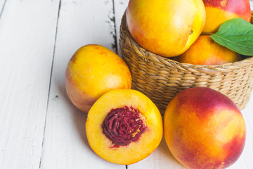 Naklejka na ściany i meble Delicious and juicy peach (nectarina) in basket on white wooden table
