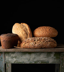 whole various baked rye flour bread rolls on an old wooden table