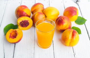 Delicious and juicy peach (nectarina) with glass of juice on white wooden table