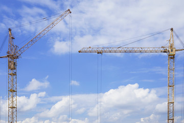 Copy space between two construction cranes against blue cloudy sky