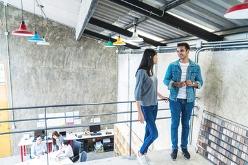 Indian happy colleagues talking while standing on top floor in modern creative office with feeling happy. Asian couple chatting, talking and discussion about work when coffee break time in morning