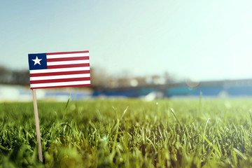 Miniature stick Liberia flag on green grass, close up sunny field. Stadium background, copy space...