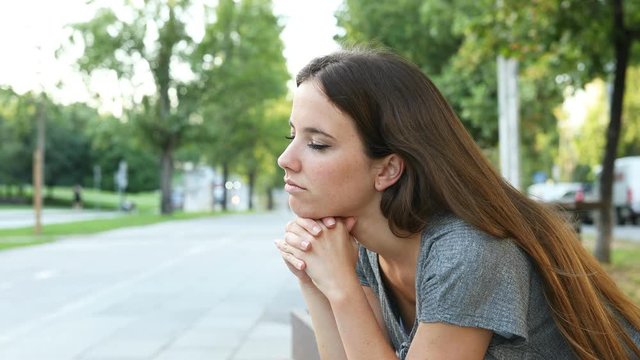 Serious pensive woman contemplating sitting on a bench in the street