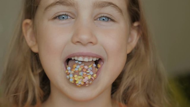 A child is smiling with a mouth full of candy. Little girl eating candy. Child eating chicle. Close up portrait silly girl with wavy hair sticking out tongue shaped candy pieces on tip.
