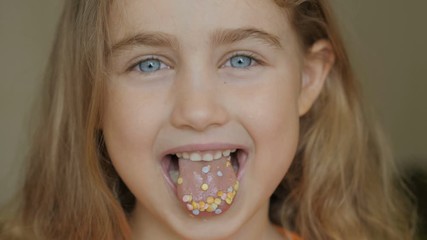 A child is smiling with a mouth full of candy. Little girl eating candy. Child eating chicle. Close up portrait silly girl with wavy hair sticking out tongue shaped candy pieces on tip.
