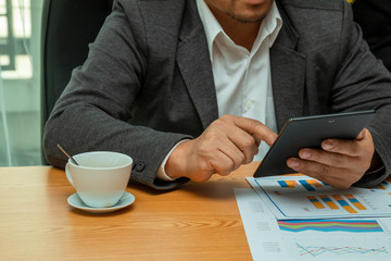 40s Asia businessman holding tablet and searching the information while checking the sales report in office