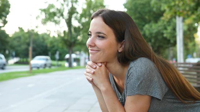 Satisfied woman thinking looking away sitting on a bench in the street