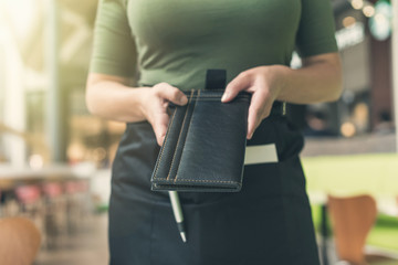 Cropped image of woman waitress in apron hold out bill folder to cafe visitor of cafe or restaurant.