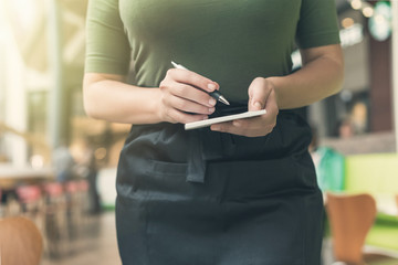 Cropped image of woman waitress in apron ready to take order using notepad and pen in cafe or restaurant.