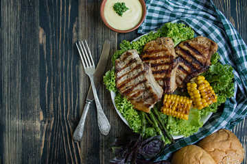 Grilled steak in a round bowl with spices, herbs and vegetables on a dark wooden background. Space for text.