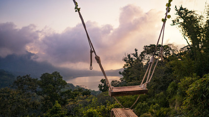 Swing on a cliff at sunset against the lake and forest