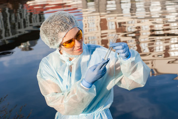 female epidemiologist looks at a test tube with water from a city river