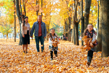 Happy family having holiday in autumn city park. Children and parents posing, smiling, playing and having fun. Bright yellow trees and leaves
