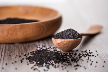 Close up shot of dried seeds of black cumin seeds kalinji on wooden spoon with wooden plate on background. Soft focus.